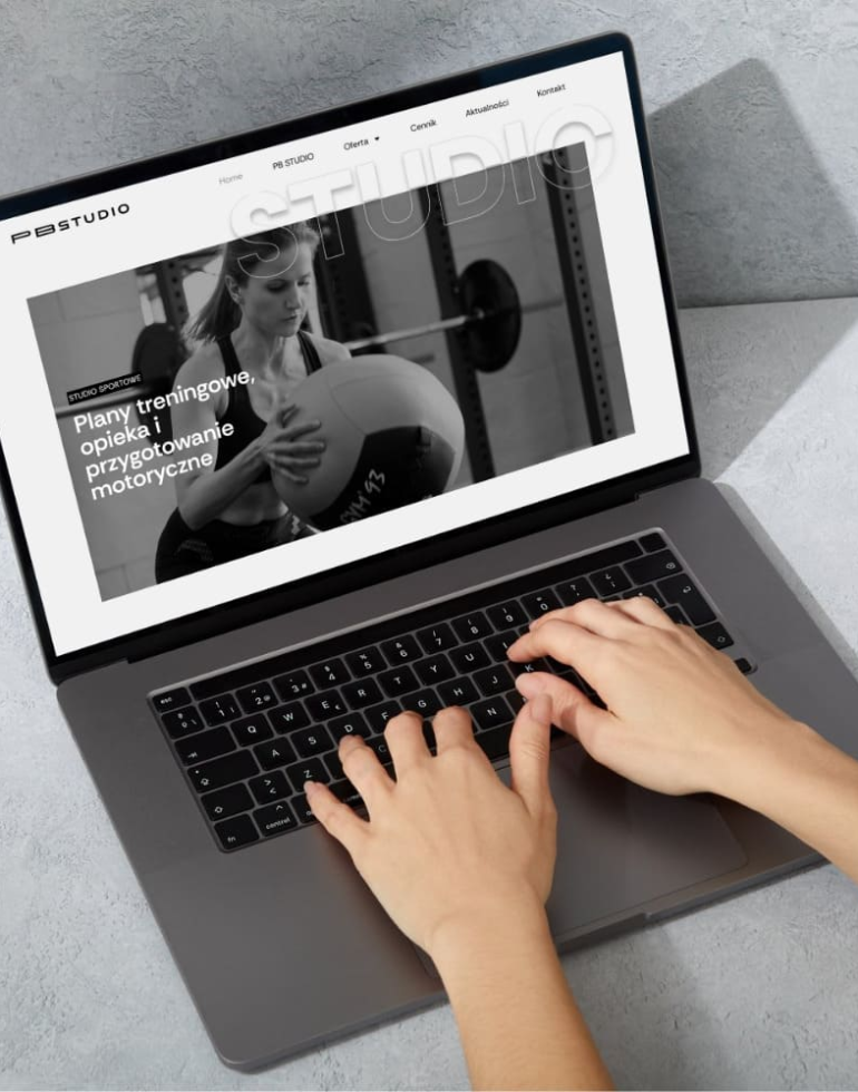 Laptop na jasnym blacie, na ekranie strona PB Studio z czarno-białym zdjęciem osoby trenującej z piłką oraz nagłówkiem Plany treningowe, opieka i przygotowanie motoryczne